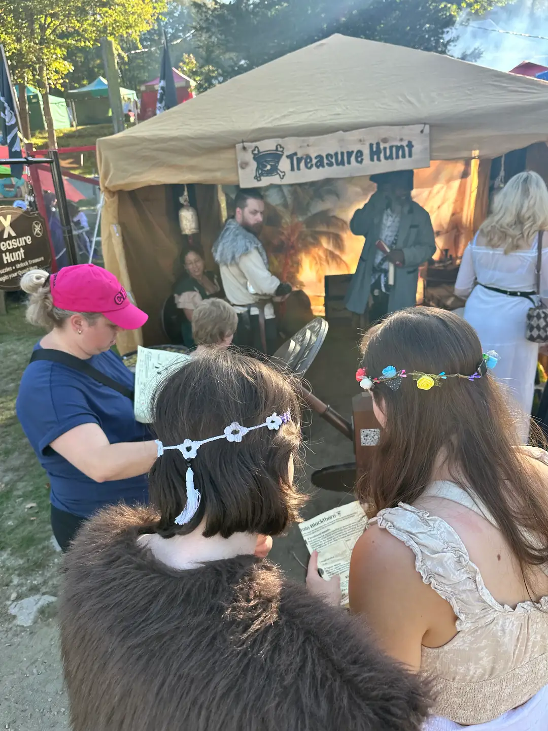 Faire-goers reading quest papers as they approach the X Treasure Hunt tent