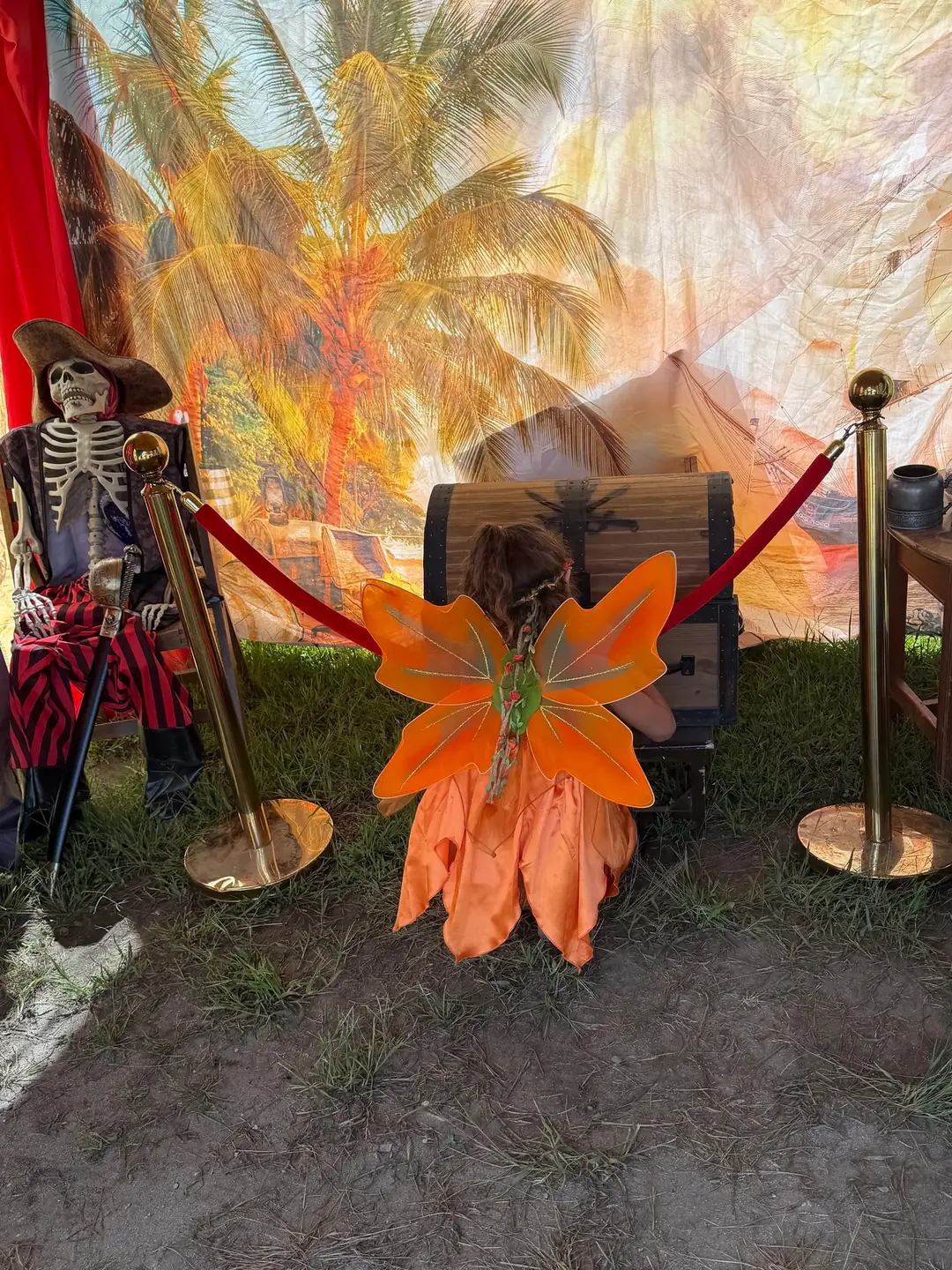 A young adventurer in orange fairy wings, seen from behind, opening the treasure chest inside the tent