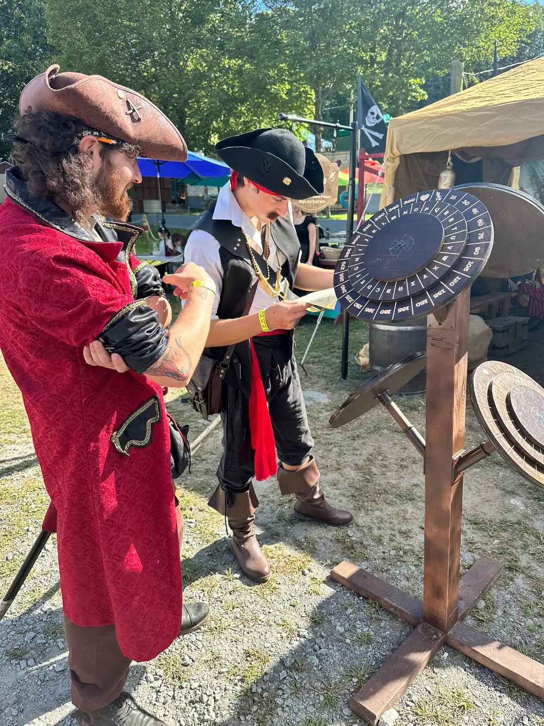 Two pirates in elaborate costumes studying a quest sheet beside the cipher wheel decoder