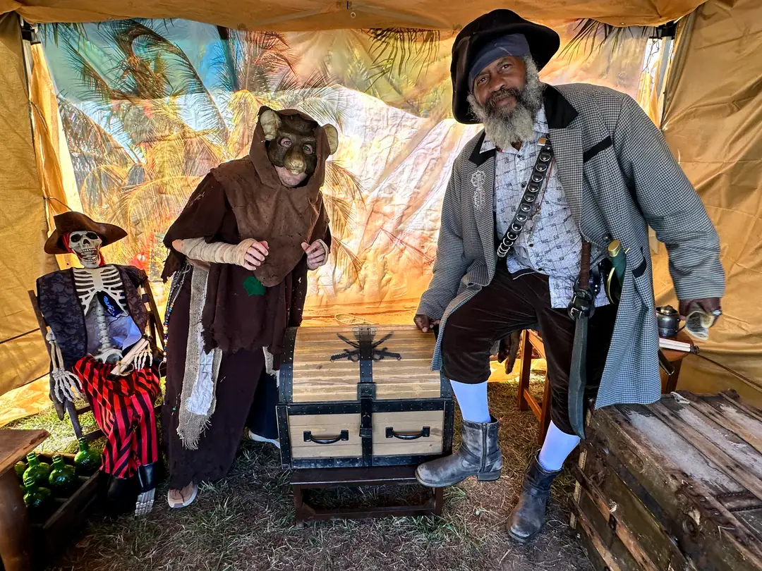 Goblin-masked visitor and pirate host inside the tropical-themed treasure tent
