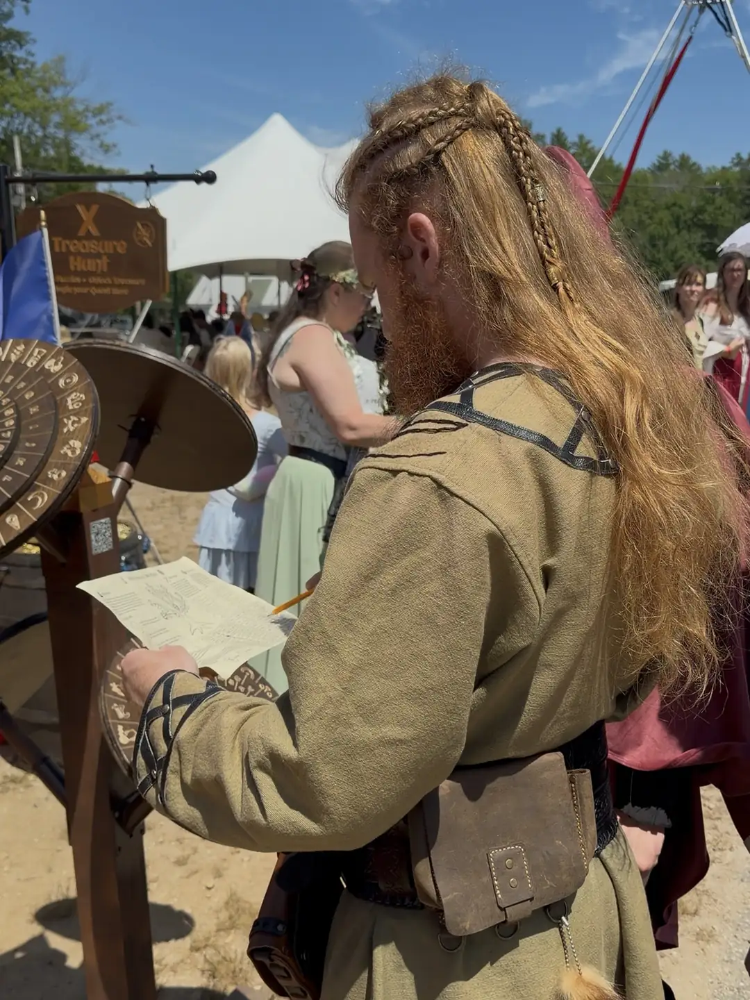 A braided Viking player reading the quest map beside the cipher wheels at the X Treasure Hunt booth