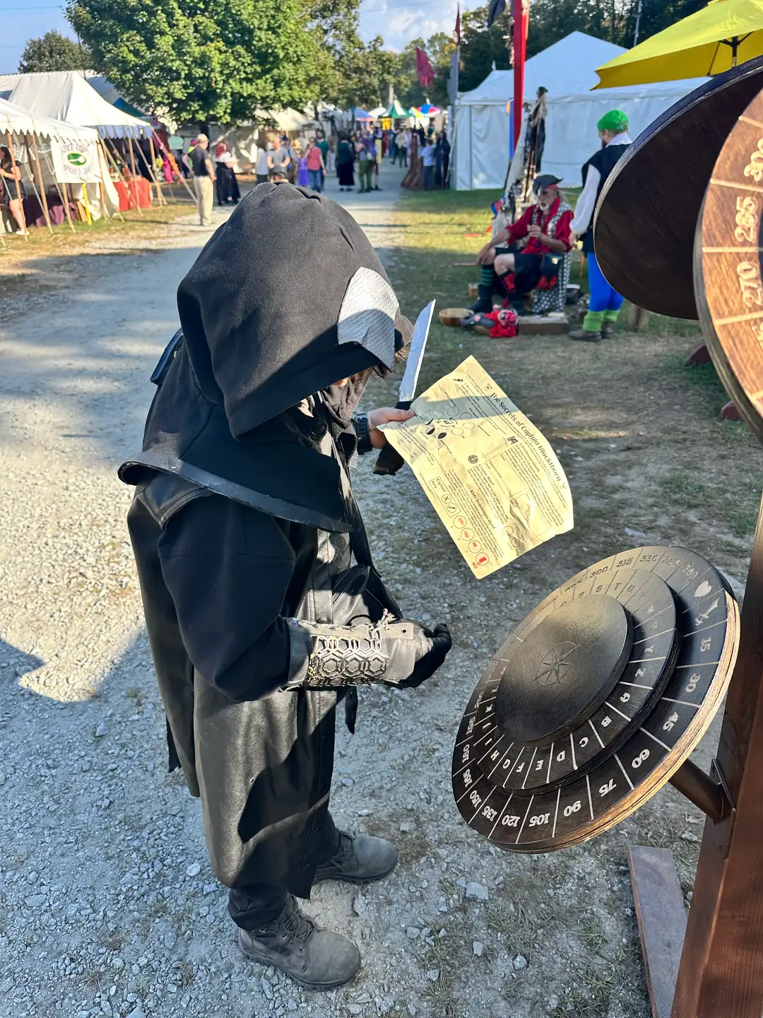 Child in dark assassin costume studying a quest sheet beside the cipher wheel