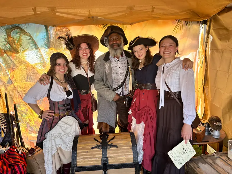 A costumed crew of five posing with the captain around the treasure chest at the X Treasure Hunt booth
