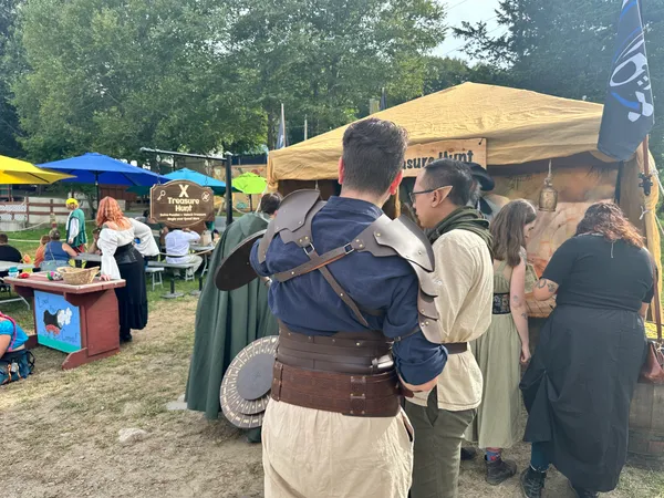 Faire-goers in Renaissance costumes lining up at the X Treasure Hunt booth