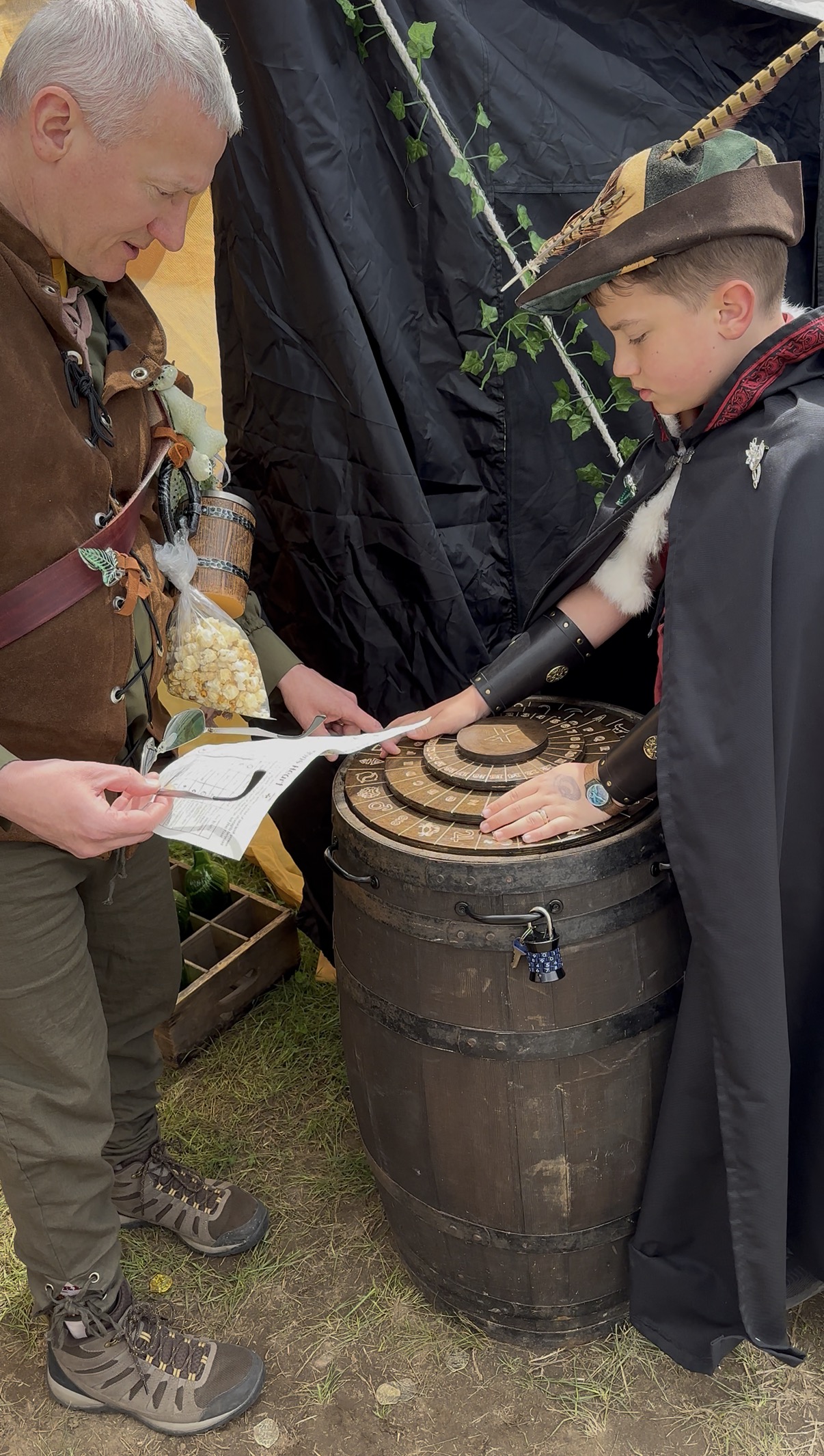 Father and son in Renaissance costumes manipulating a cipher disc on a padlocked barrel