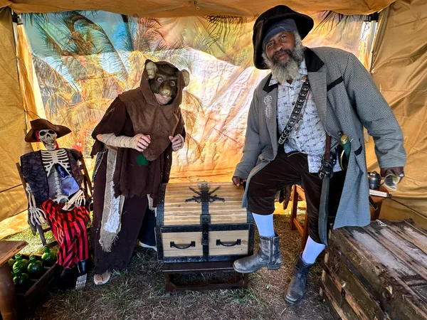 Goblin-masked visitor and pirate host inside the tropical-themed treasure tent