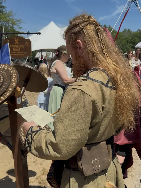 A braided Viking player reading the quest map beside the cipher wheels at the X Treasure Hunt booth