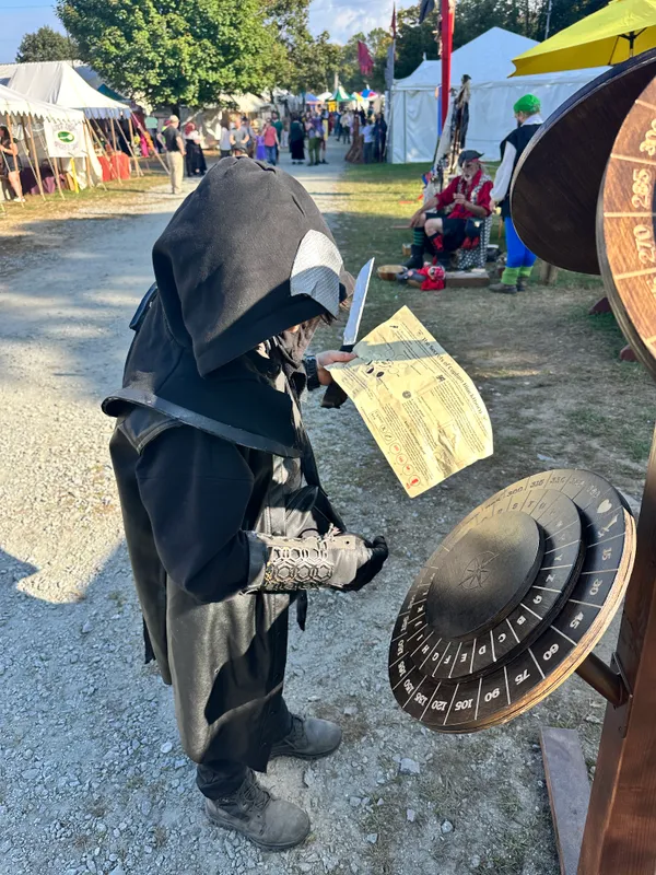 Child in dark assassin costume studying a quest sheet beside the cipher wheel