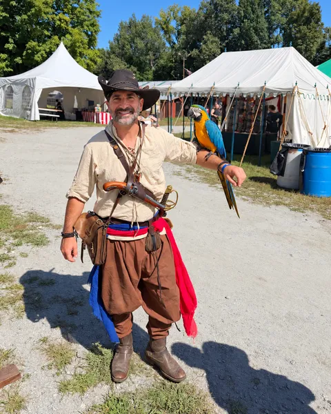 Tino, founder of X Treasure Hunt, in pirate costume with a blue-and-gold macaw at the faire